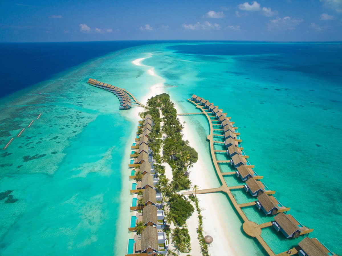 Aerial view of a sandbar lined with overwater villas surrounded by turquoise ocean, showcasing luxury all-inclusive Maldivian vacation getaways.