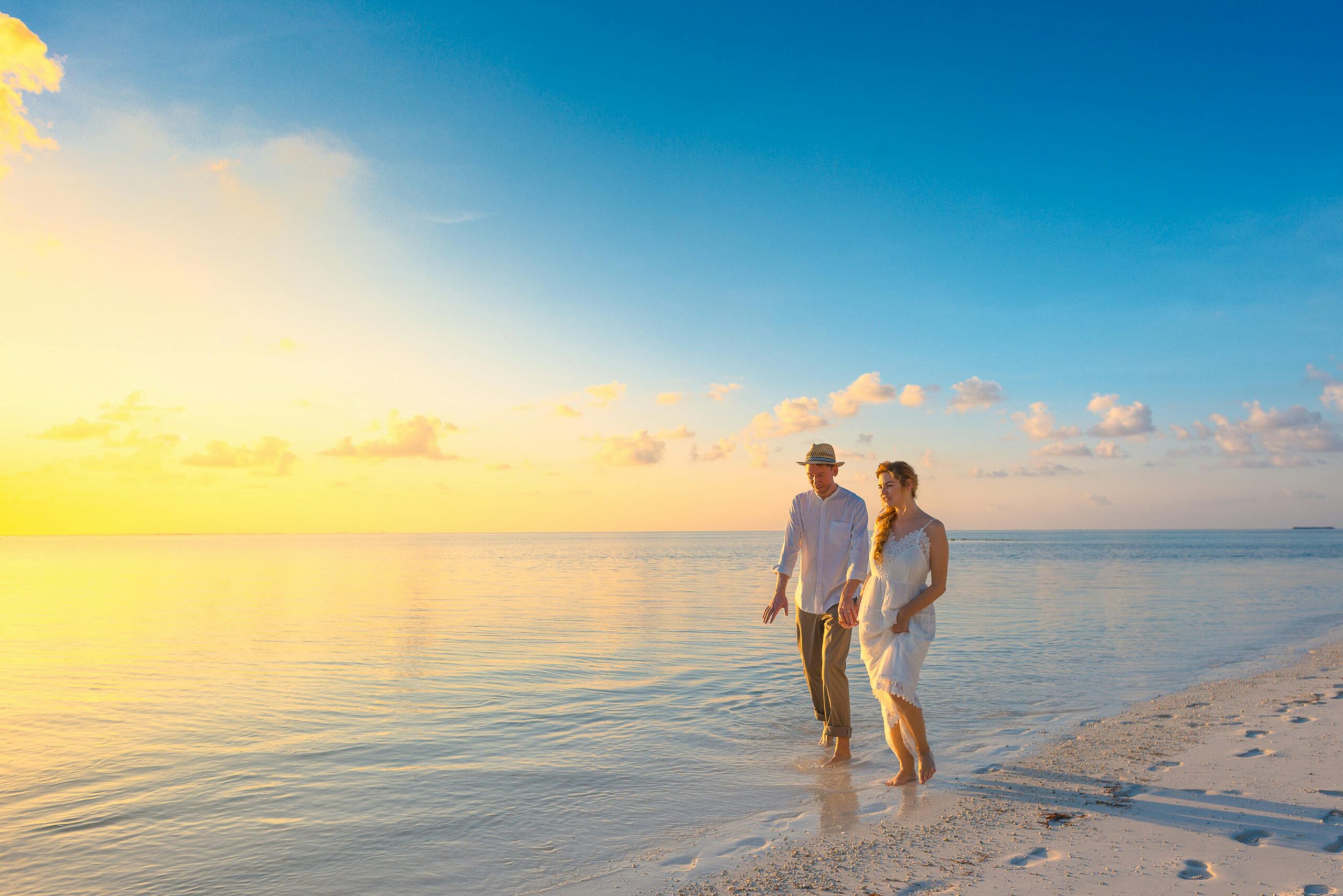 Couple walking together on a Maldives beach at sunset, symbolizing romantic honeymoons and all-inclusive getaway packages.