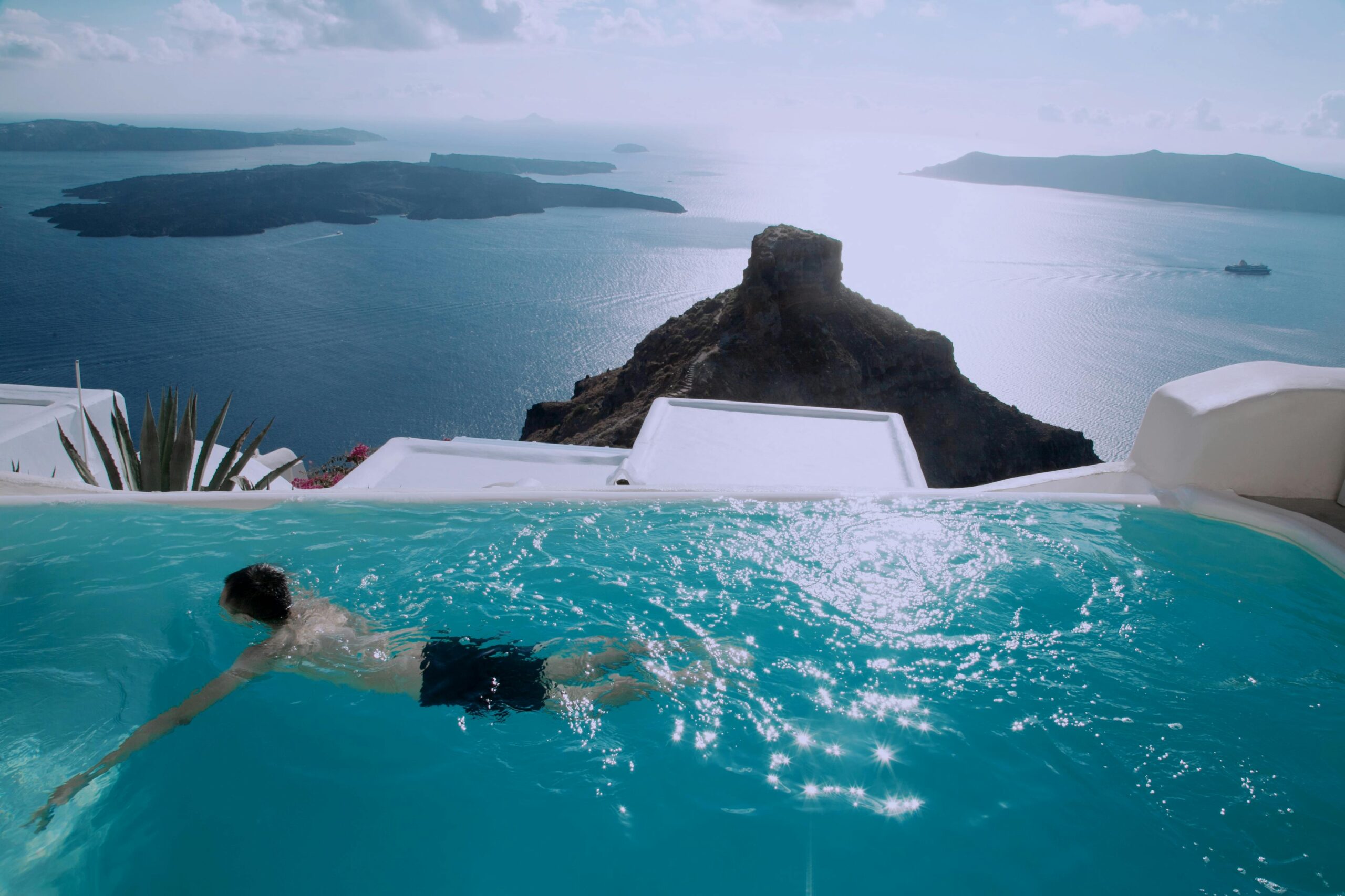 Balcony pool overlooking Santorini’s hillside homes and the Mediterranean, showcasing luxury all-inclusive resort vacations.