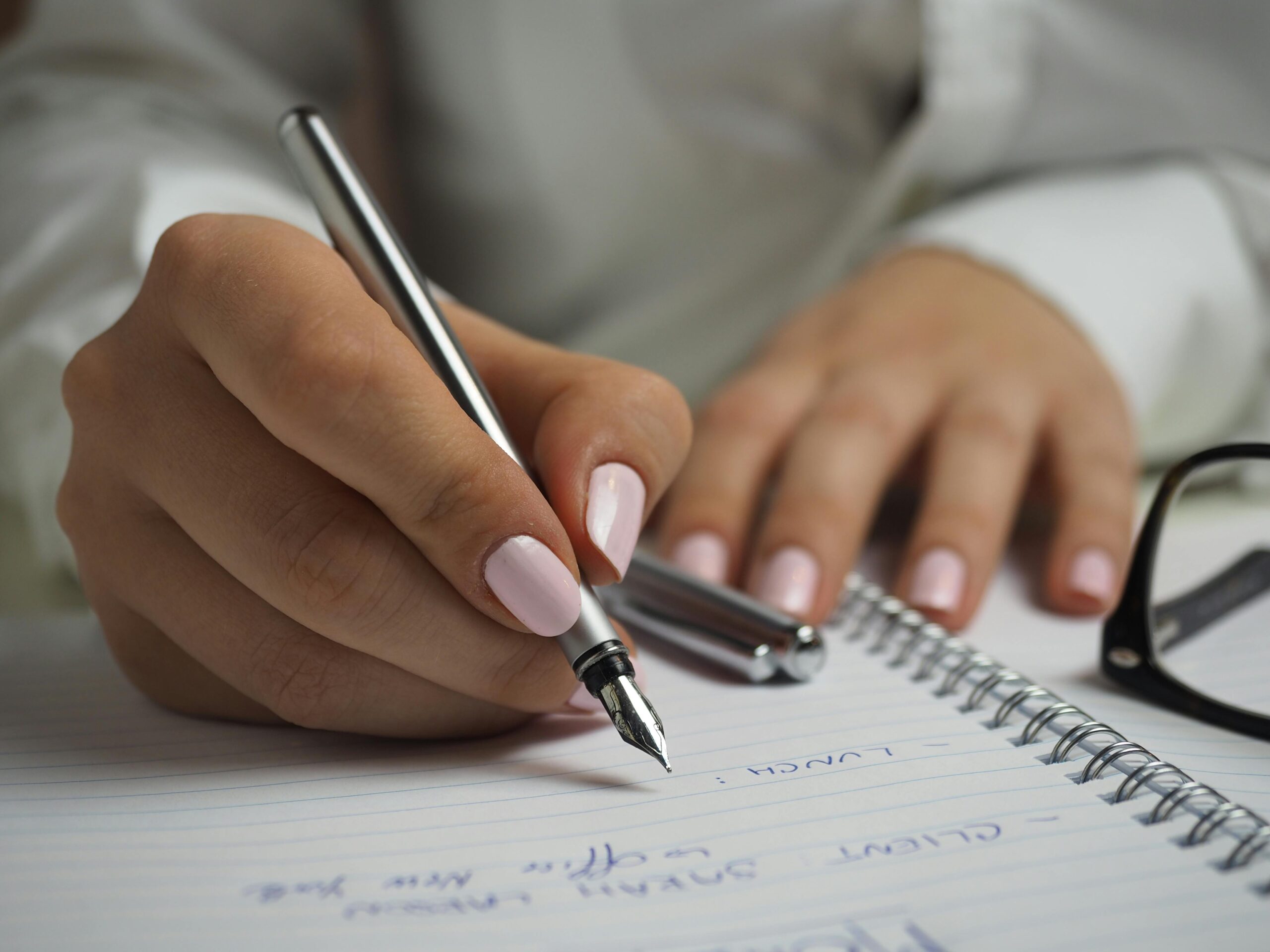Person writing notes in a spiral notebook, representing travel planning and itinerary preparation services.